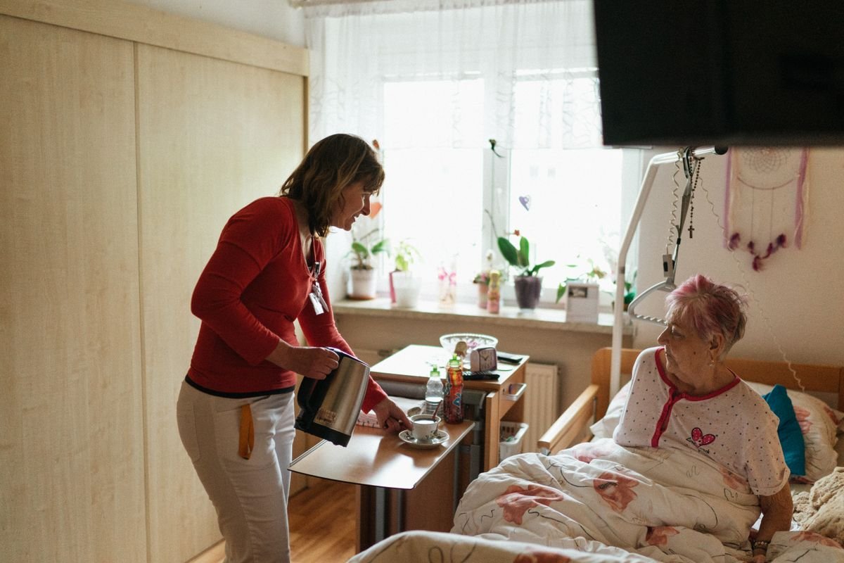 Cuidadora serve chá a uma senhora acamada no quarto de casa